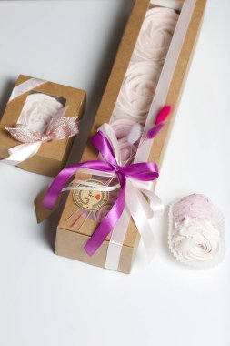 Kağıt ambalajda marşmelov. Kurdelelerle ve kurumuş çiçeklerle süslenmiş. Gül şeklinde bir Zephyr. Beyaz arkaplanda.