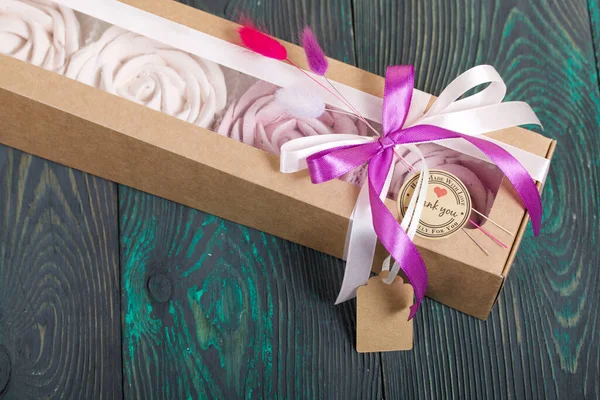 Marshmallows in craft paper packaging. Decorated with ribbons and dried flowers. Zephyr in the form of a rose. On painted pine boards.