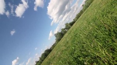 Yeşil çimenli çayır. Bulutlu mavi gökyüzü. Güneşli havada yaz manzarası. Yatay eksende kamera döndürmesi.