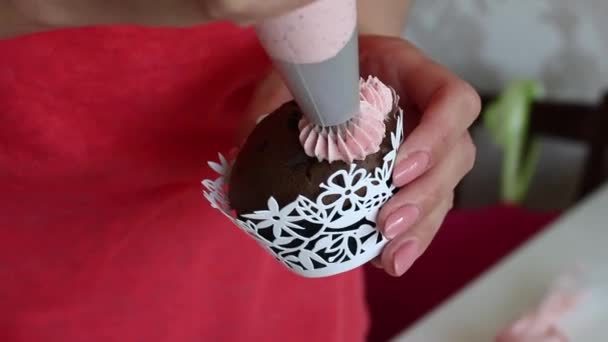 Menina está preparando cupcakes de chocolate com creme de morango. Aplica a nata de um saco de massa. Imagem de close-up . — Vídeo de Stock