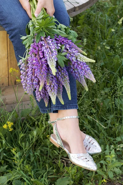 Female legs in summer sandals and a bouquet of lupine. Close-up shot.