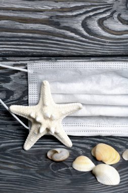 Deniz yıldızı ve deniz kabukları siyah ve beyaza boyanmış çam ağaçlarına saçılmıştır. Yakınlarda tıbbi bir maske var. Denizde tatil 2020.