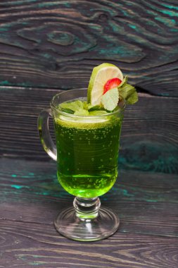 Bardakta yeşil limonata. Limon ve çilekle süslenmiş. Bir tutam nane şekeriyle. Çam ağacında.