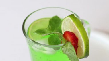 Limonata yeşildir. Limon, çilek ve nane yapraklarıyla süslenmiş. Kadın onu yana çeviriyor..