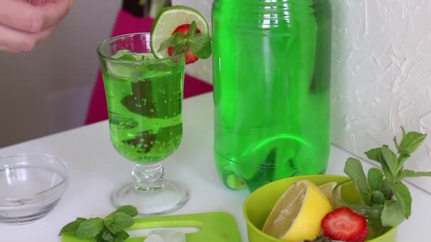 La limonada es verde. Decorado con lima, fresas y hojas de menta. Una mujer le añade un trozo de hielo — Vídeo de stock