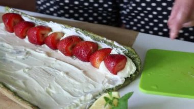 Bir kadın kremalı ve çilekli bir sünger keki bir tüpe sarar. İsviçre rulosu yapma süreci.