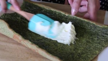 Bir kadın üzerine ıspanak ve nane eklenmiş bisküvi ile krema sürer. İsviçre rulosu yapma süreci.