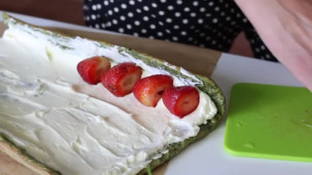 La torta de esponja con la adición de espinacas y menta se extiende con crema. Una mujer le pone fresas para llenarlas. El proceso de hacer rollo suizo . — Vídeo de stock