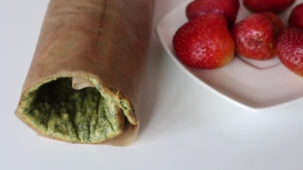 Pastel de galletas al horno enrollado en un tubo. Cerca están los ingredientes para el relleno. El proceso de hacer rollo suizo . — Vídeo de stock