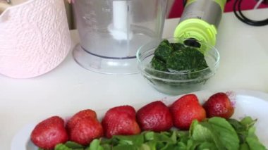 Bir kadın hamuru mikserle karıştırıyor. İsviçre dürümünün hazırlığı için. Masanın yanında malzemeler var. Çilek, nane ve daha fazlası.