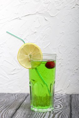 Bardakta yeşil limonata. İçinde kiraz yüzüyor. Bir dilim limonla süslenmiş. Kokteyl yerine pipetle.
