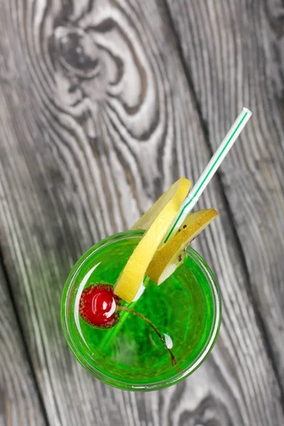 Green lemonade in a glass. Cherry floats in it. Garnished with a slice of lemon. With a straw for a cocktail.