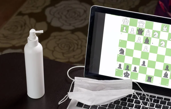 Chess task on laptop screen online. Near antibacterial spray and medical mask. Leisure in self-isolation. International chess day.