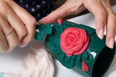 Kadın, polimer gülleri kupaya yapıştırıyor. Farklı renklerde polimer kil. Polimer kil el sanatları.