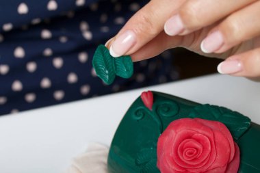 Kadın, polimer gülleri kupaya yapıştırıyor. Farklı renklerde polimer kil. Polimer kil el sanatları.