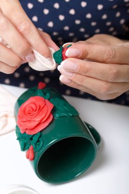 Kadın, polimer gülleri kupaya yapıştırıyor. Farklı renklerde polimer kil. Polimer kil el sanatları.