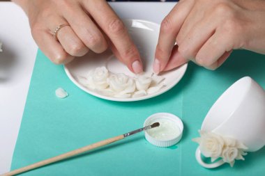 Beyaz polimer kil yapraklı güller. Bir kadın onları bir tabağa yapıştırıyor. Polimer kil el sanatları.