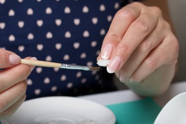 Beyaz polimer kil yapraklı güller. Bir kadın onları bir tabağa yapıştırıyor. Polimer kil el sanatları.