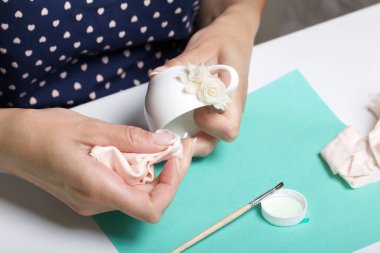 Beyaz polimer kil yapraklı güller. Bir kadın bardağa yapıştırıyor. Polimer kil el sanatları.