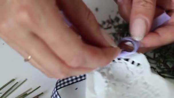 Uma mulher está embrulhando flores de lavanda em papel artesanal. Amarra a cassete. Na mesa estão flores de lavanda e acessórios . — Vídeo de Stock