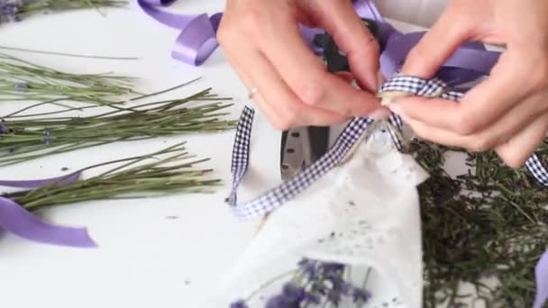 Una mujer está envolviendo flores de lavanda en papel artesanal. Vendajes de la cinta. Sobre la mesa hay flores de lavanda. . — Vídeos de Stock