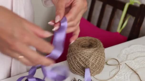 Mulher a enfaixar uma fita de lavanda. Buquê em papel artesanal. Na mesa estão flores de lavanda e acessórios . — Vídeo de Stock