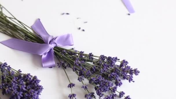 Na mesa estão flores de lavanda. Uma mulher está embrulhando flores de lavanda em papel artesanal. Ligaduras a fita . — Vídeo de Stock