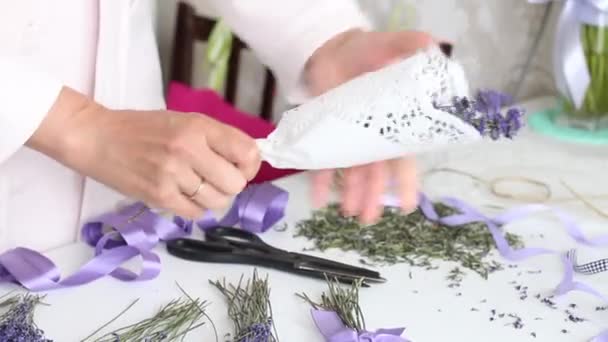 Uma mulher está embrulhando flores de lavanda em papel artesanal. Na mesa estão flores de lavanda . — Vídeo de Stock