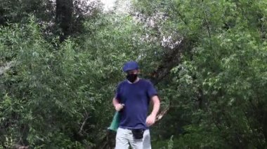 Maskeli bir adam nehir kıyısında yürüyor. Omzunda kamp sandalyesi taşıyor. Salgın ve kendini soyutlama süresince yürüyüş ve dinlenme. Yakın plan..