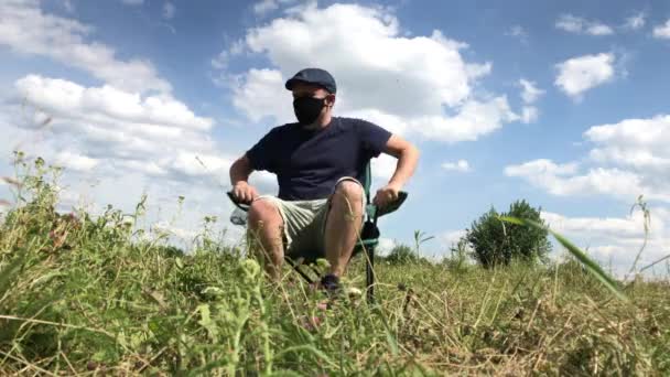 Un hombre enmascarado se sienta en una silla de camping. Salí a tomar aire fresco en el parque de la ciudad. Caminar y descansar durante la epidemia y el autoaislamiento. Plan global . — Vídeo de stock