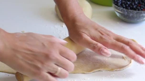 Uma mulher distribui a massa para fazer bolinhos. Próximo na mesa são mirtilos para enchimento — Vídeo de Stock