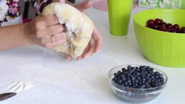 Una donna si impasta la pasta nelle mani per fare gnocchi. Avanti sul tavolo ci sono mirtilli e ciliegie per il ripieno. — Video Stock