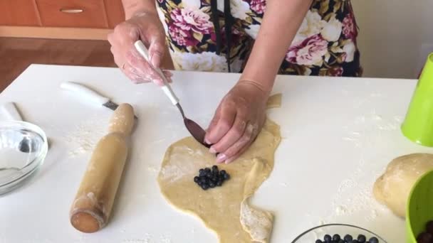 Uma mulher prepara bolinhos com mirtilos. Coloca bagas em massa enrolada — Vídeo de Stock