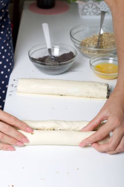 Bir kadın cevizli puf böreğini tüpe sarar. Haşhaş ve ceviz dolgulu bukleler yapmak için. Masanın yanında malzemeler ve aletler var..