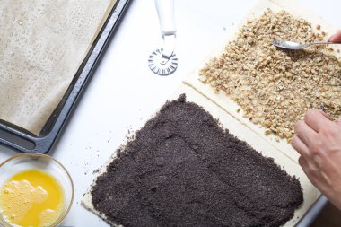 Bir kadın fındıklı börek serpiyor. Haşhaş ve ceviz dolgulu bukleler yapmak için. Masanın yanında malzemeler ve aletler var..