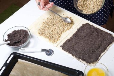 Bir kadın fındıklı börek serpiyor. Haşhaş ve ceviz dolgulu bukleler yapmak için. Masanın yanında malzemeler ve aletler var..