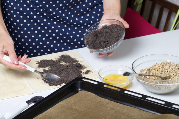 Woman sends poppy seeds puff pastry. For making puff pastry curls with poppy and walnut filling. Nearby on the table are ingredients and tools.