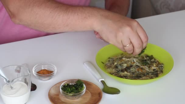 L'uomo mette un piatto di zuppa di acetosa sul tavolo. Aggiunge aneto, spezie e panna acida ad esso. Prodotti alimentari regionali — Video Stock