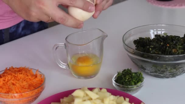 The man knocks the eggs into a glass and mixes with a fork. Nearby are potatoes, carrots and sorrel. For making sorrel soup. Regional food. — Stock Video