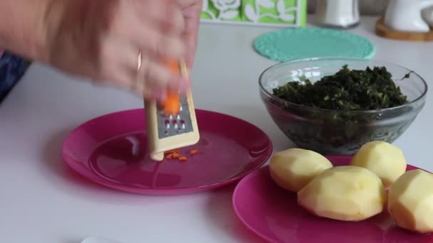 En man hugger morötter i en tallrik. I närheten finns potatis och sorrel. För att göra soppa. Regional mat. Närbild. — Stockvideo