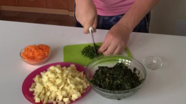 Bir adam dereotu kesme tahtasına koyar ve bir konteynıra koyar. Yakınlarda patates, havuç ve kuş var. Kuş çorbası yapmak için. Bölgesel gıda.