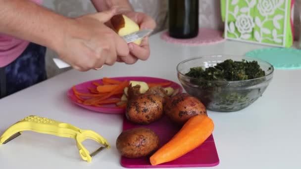 De man schilt aardappelen. Vlakbij zijn wortelen en zuring. Voor het maken van zuring soep. Regionaal voedsel — Stockvideo