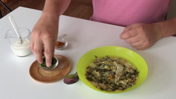 Ο άνθρωπος βάζει ένα πιάτο σούπα σόρελ στο τραπέζι. Προσθέτει άνηθο, μπαχαρικά και ξινή κρέμα σε αυτό. Τοπικά τρόφιμα. — Αρχείο Βίντεο