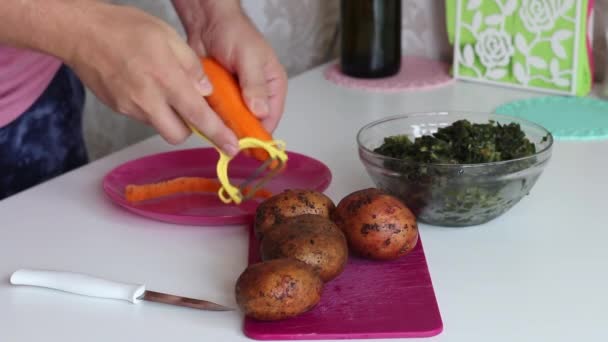 El hombre está pelando zanahorias. Muy cerca hay papas y acedera. Para hacer sopa de acedera. Alimentación regional . — Vídeo de stock