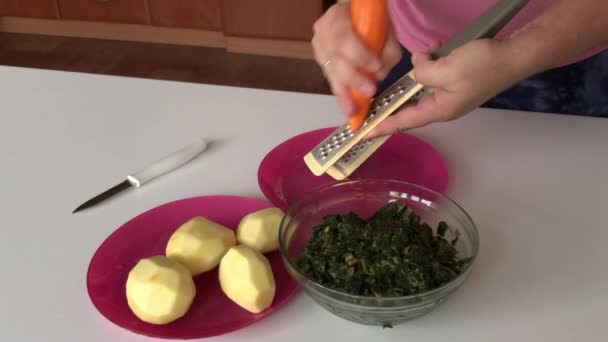 Han slipar morötter. I närheten finns potatis och sorrel. För att göra soppa. Regional mat. — Stockvideo