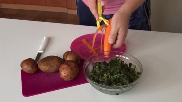 Чоловік очищає моркву. На столі лежить картопля і щавлю. Для виготовлення борошняного супу . — стокове відео