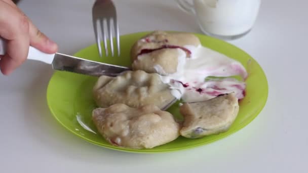 Dumplings with sour cream are on the plate. The man cuts off a piece, dips it in sour cream and tastes it. The cherry filling is visible. — Stock Video