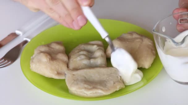 Egy férfi tejfölt tesz egy tányér kész gombócra.. — Stock videók