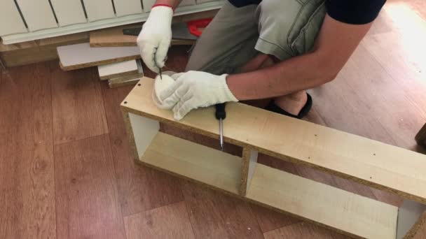 L'homme assemble le cadre de l'étagère et ses pièces. Lubrifie la vis autotaraudeuse avec du savon et la transforme en planche. Fabrication de meubles à la maison. — Video