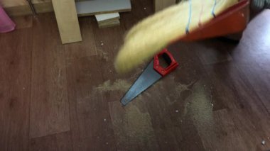 Bir adam yerden süpürgeyle talaş topluyor. Evde mobilya yapmak.